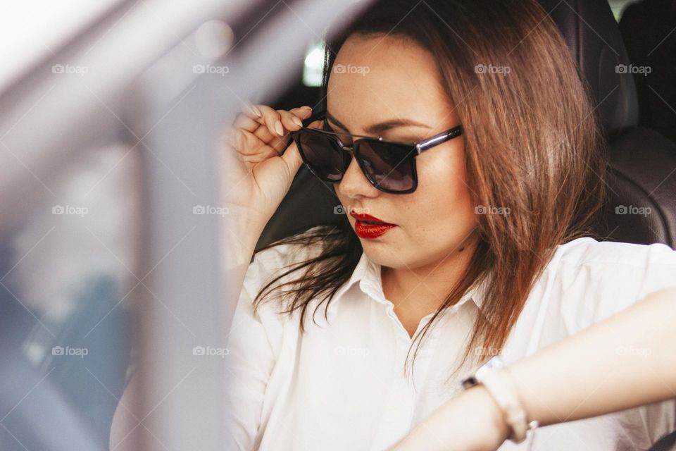 Beautiful successful elegant brunette young woman with red lips in sunglasses driving the passenger car