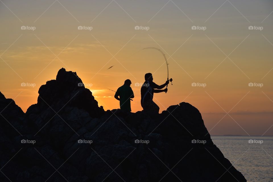 Silhouette of two boys fishing during sunset