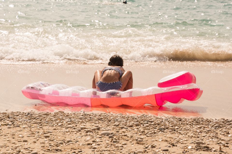 A little girl playing on the beach sitting on her air bed