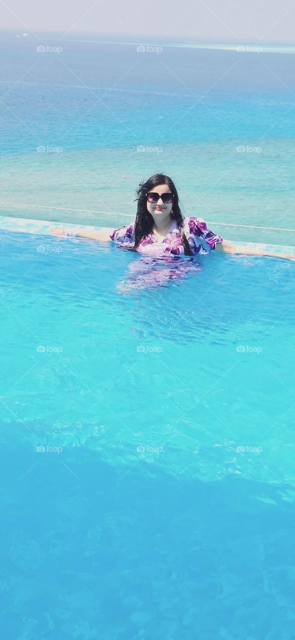 Surrounded by the calming blue waters,this mother enjoying a peaceful moment.The gentle lapping of the waves and the sparkling pool create a serene backdrop,perfectly complimenting her contented smile.