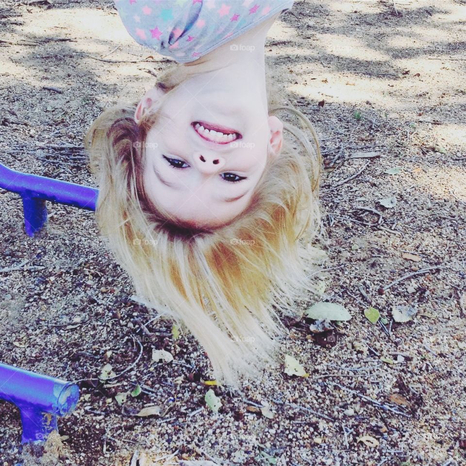 Little girl hanging upside down on monkey bars at the park.