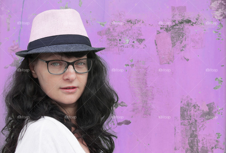 Portrait of beautiful woman with glasses and hat against pink colored metal wall