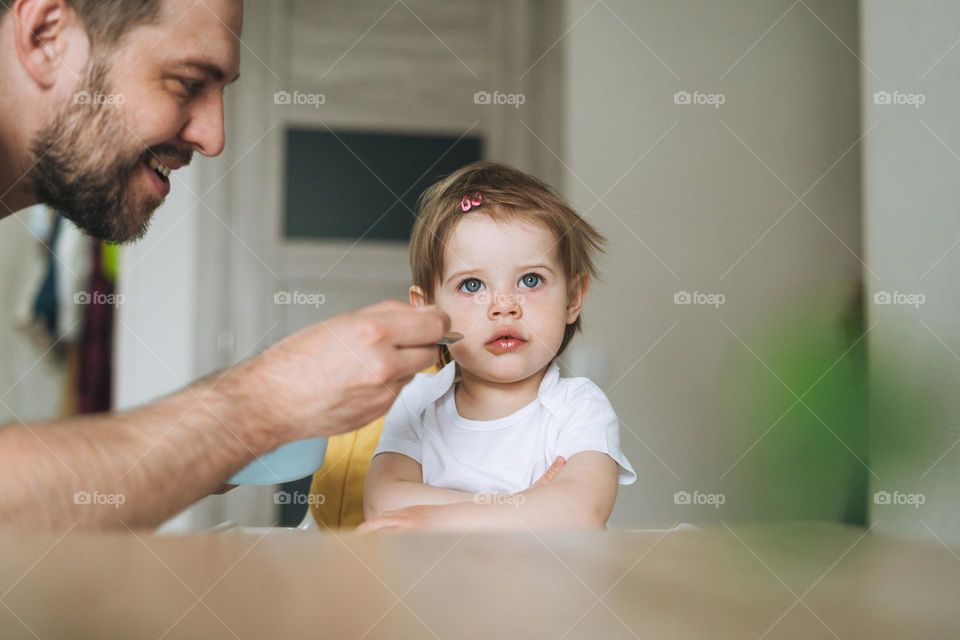 Father young man feeds baby girl little daughter in kitchen at home