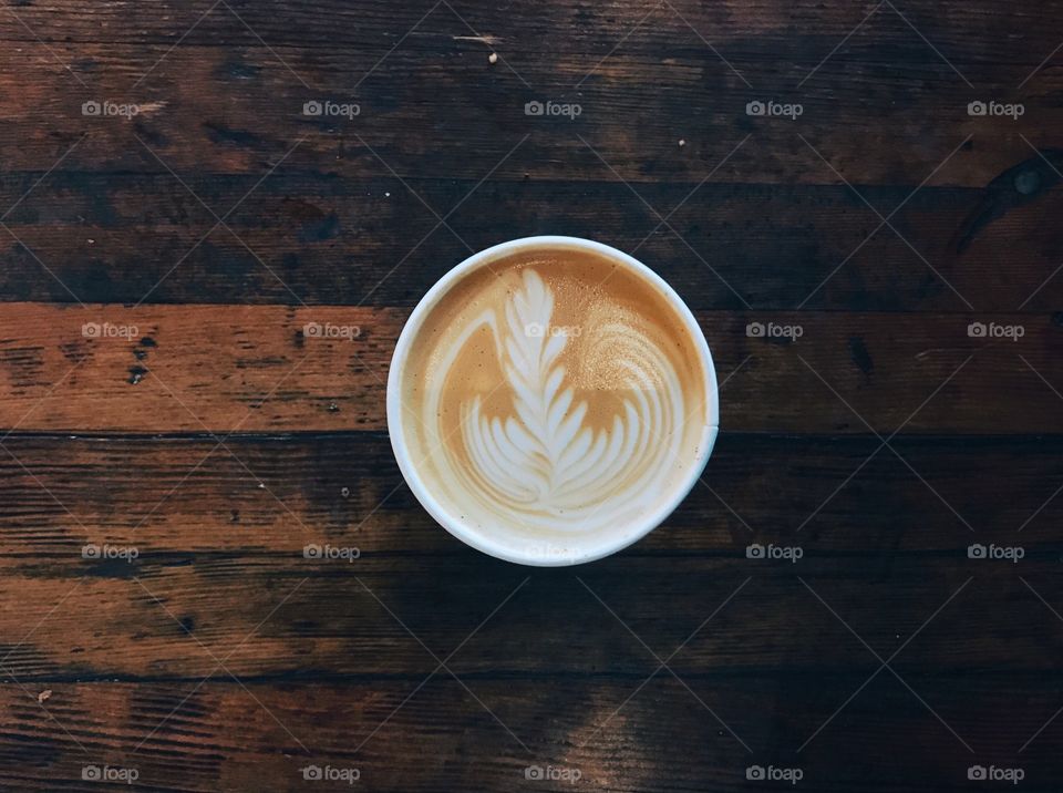 Overhead cafe shot of a cappuccino on a rustic wood farmhouse table.