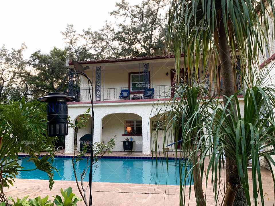 White and red spanish old style architecture residential large house built in the early 1900s. Charming pretty style and beautiful landscaping with pool and chairs with great setting in a tropical environment.