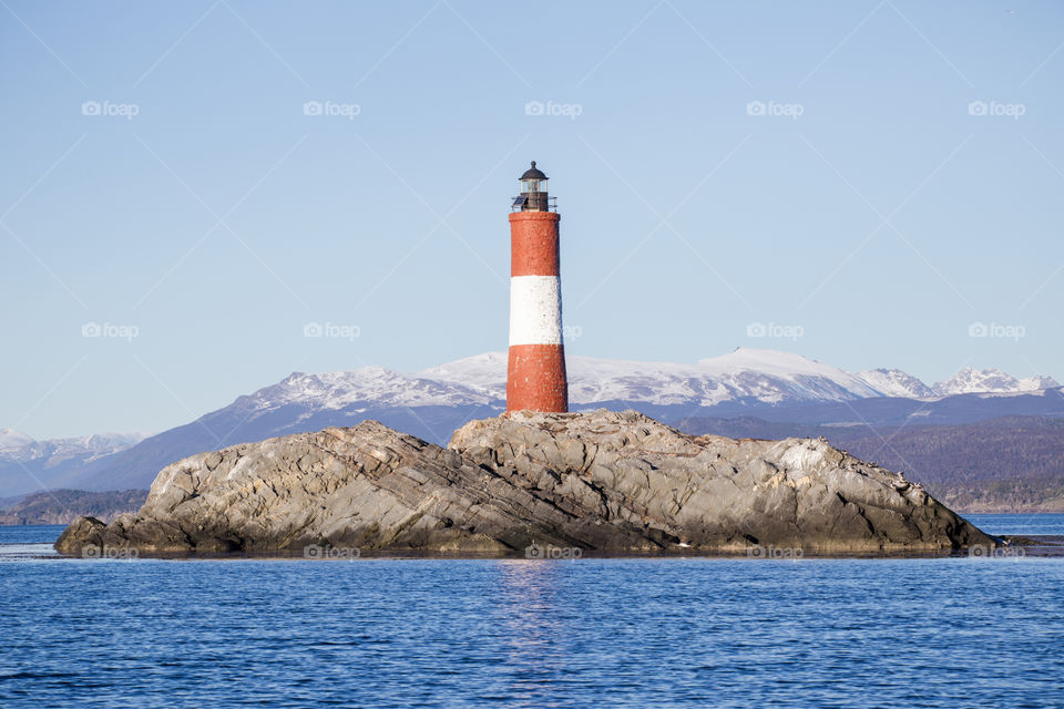 lighthouse on an island with snowy mountains at the back