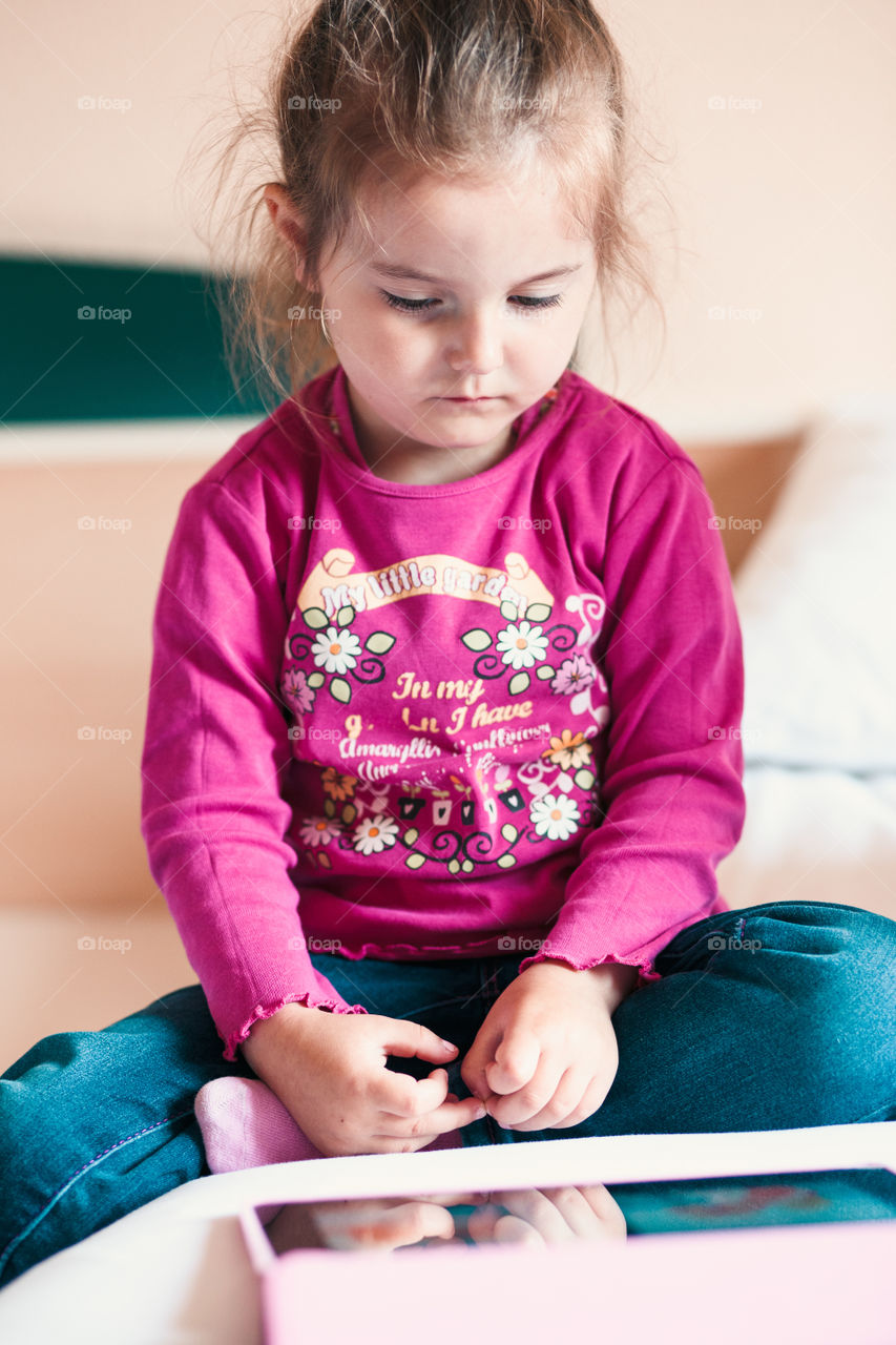 Little girl watching a animated movie for kids on tablet, sitting in bed in bedroom