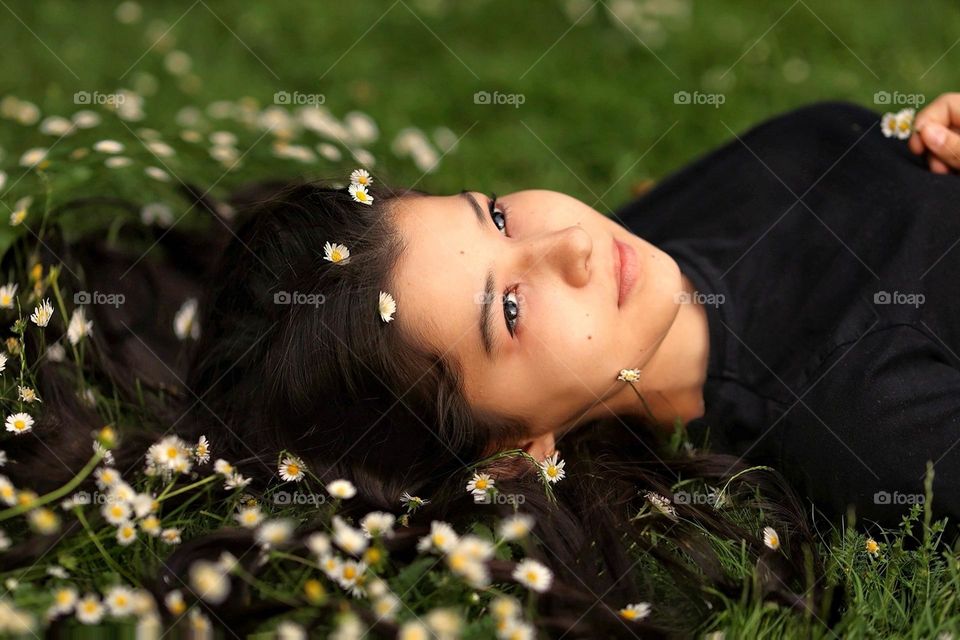 All women's are natural beautiful without any cosmetic. Young woman with lovely long hair and white daisies lies in the green grass. Natural womаn, natural beauty.