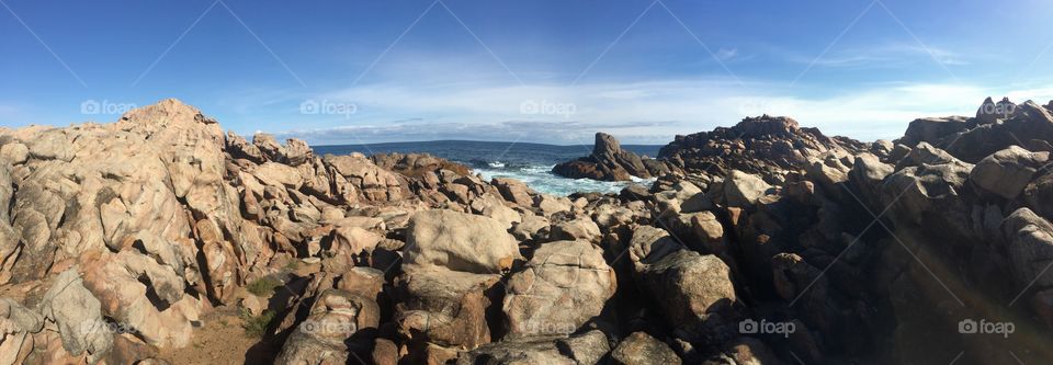 Panoramic view of coastline with rocks, ocean and blue sky 