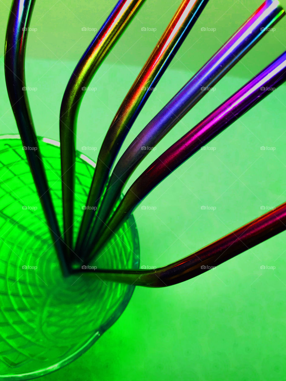 Rainbow metal straws splayed out in a green fluted & textured glass on a green background. 