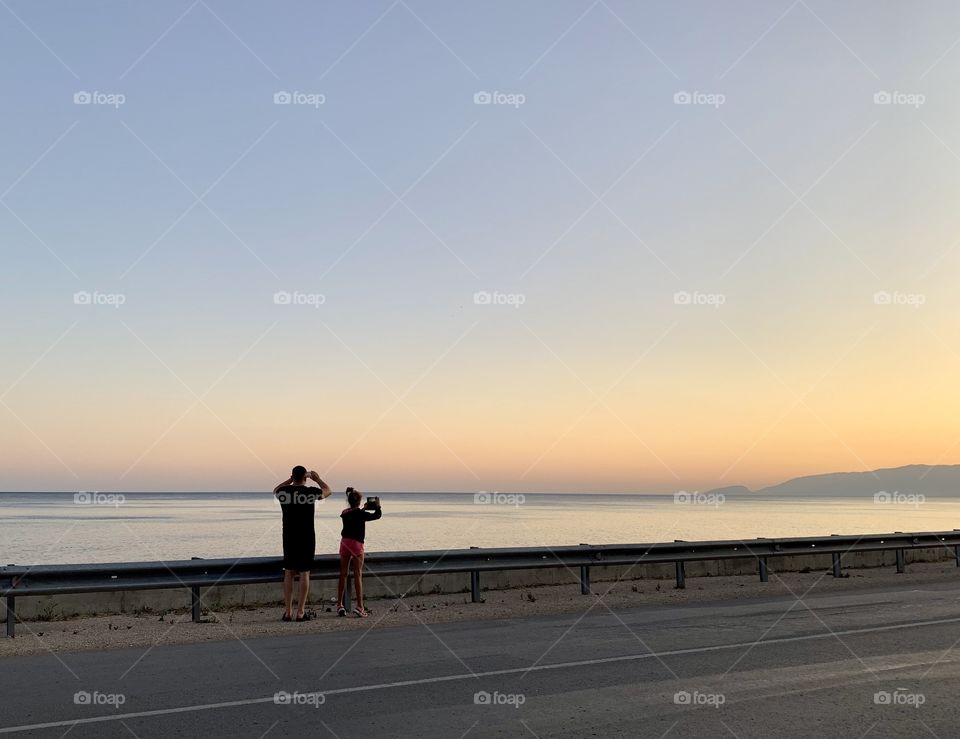 Dad and daughter are photographing the sunset in the mountains. Summer holidays. road to the sea.