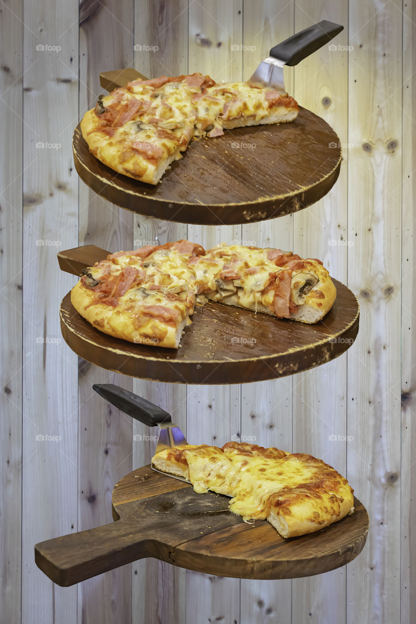 Pizza with ham and cheese on the wooden tray is placed on a wooden background