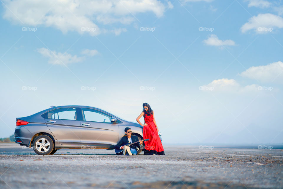 Woman leaning on car looking at man playing guitar