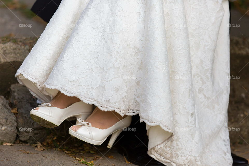 White wedding dress  and groom black suit and white shoes sitting on stone steps