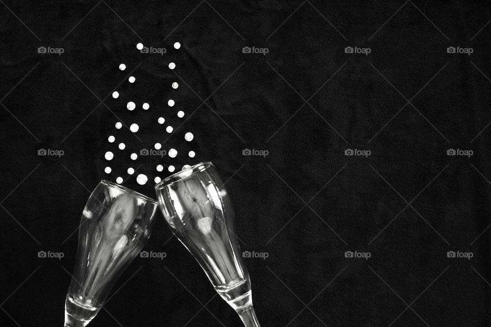 Flat lay of champagne glasses and  rhinestone bubbles on black background in black and white