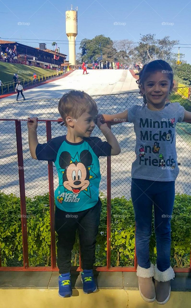 As it doesn't snow in Brazil, we don't have ice or snow for winter sports.  The solution was to build an artificial ski slope. In the photo, two children in front and in the back, artificial ski slope, cable car and skiers practicing the sport.