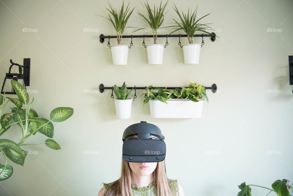 Young millennial woman wearing a virtual reality headset indoors surrounded by plants