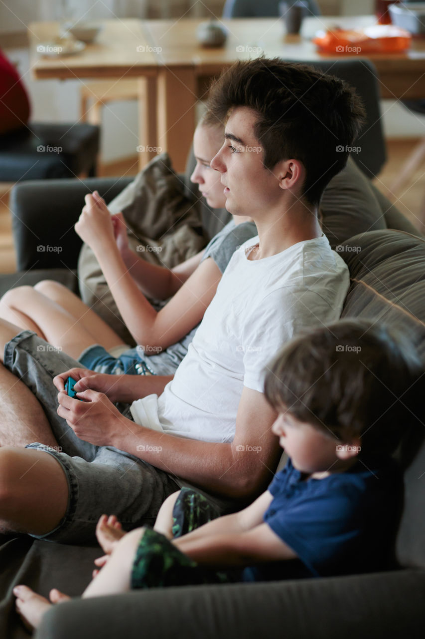Concentrated young boy and girl playing video games sitting on sofa at home