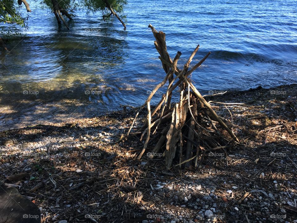 Stack of sticks, kindling and logs prepared for summertime camping cookout and camp fire next to lake with willow tree hanging over water healthy outdoor activity and lifestyle photography