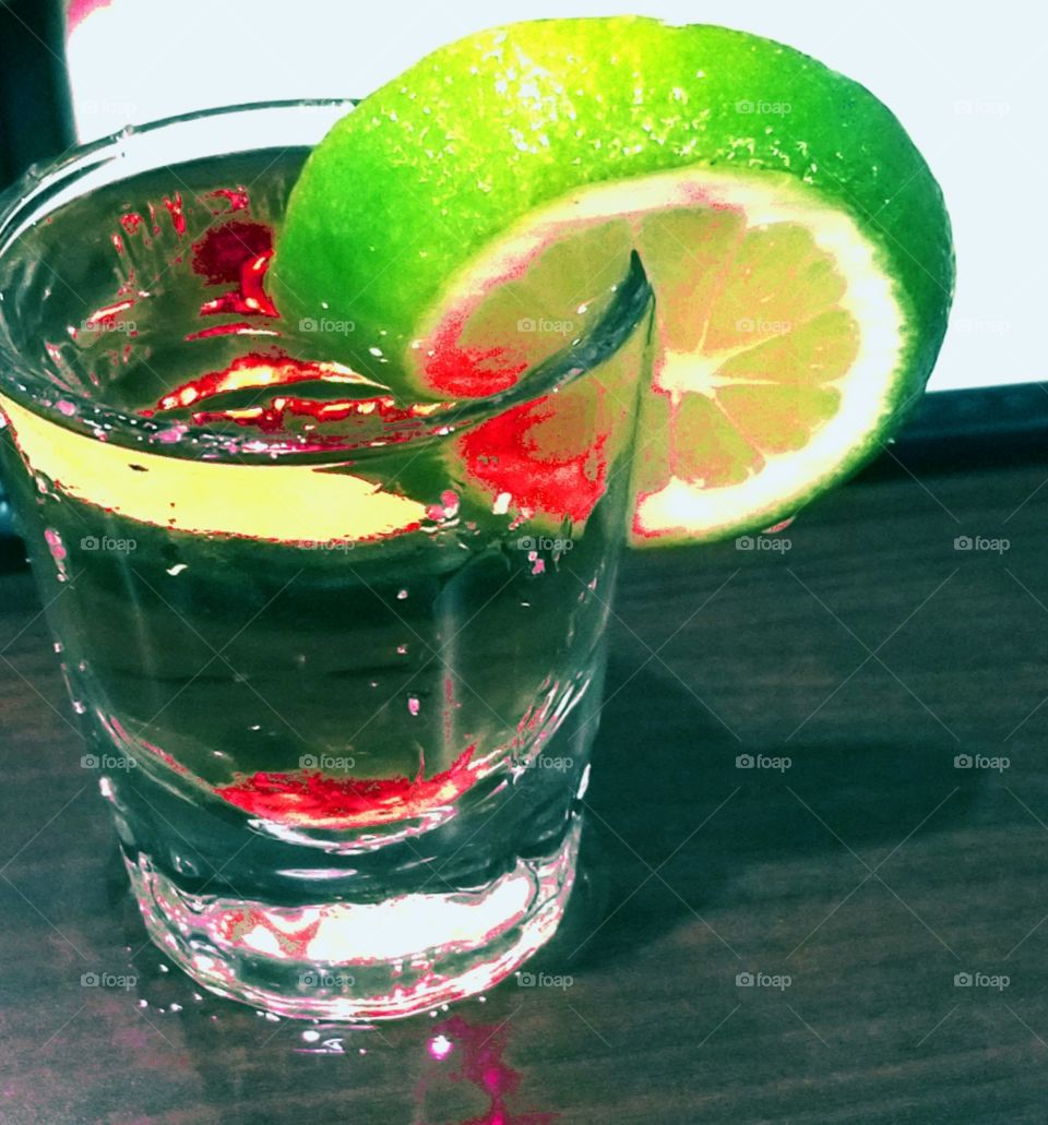Quenching gold tequila shot with bright green lime wedge garnish on summer day!