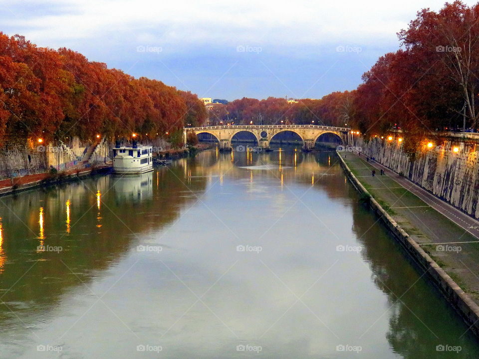bridge trees and boat reflecting into the water in the autumn season - Tevere river