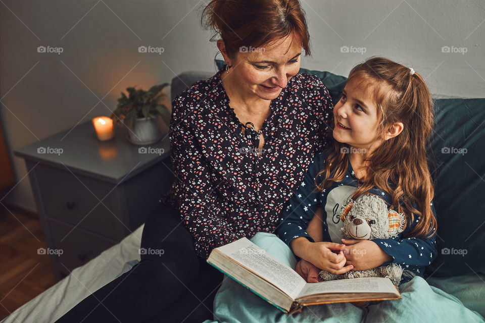 Mother reading book her daughter in bed before going to sleep. Reading stories before sleep. Bedtime stories for child