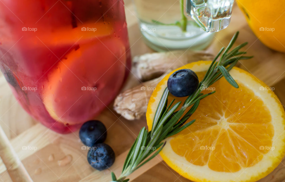 Aromatic and healthy summer drink on dark wood tray with ingredients for wellbeing and healing are ginger root, antioxidant blueberry, aromatic rosemary, mint herb and vitamin rich sliced orange 