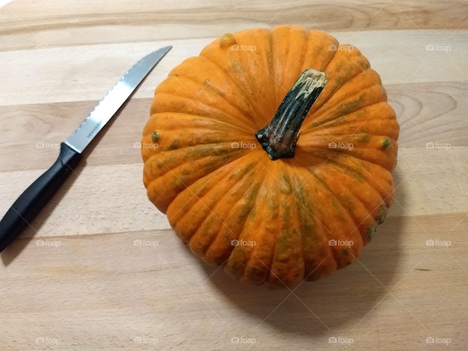 large pumpkin on wooden cutting board with knife ready to prepare for cooking
