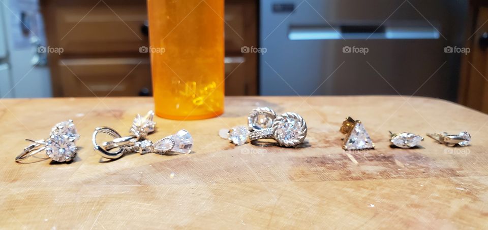 Earrings, Shiney earrings, all different shapes & sizes of diamonds laid out with remainder in pill bottle. Out for cleaning and drying.
