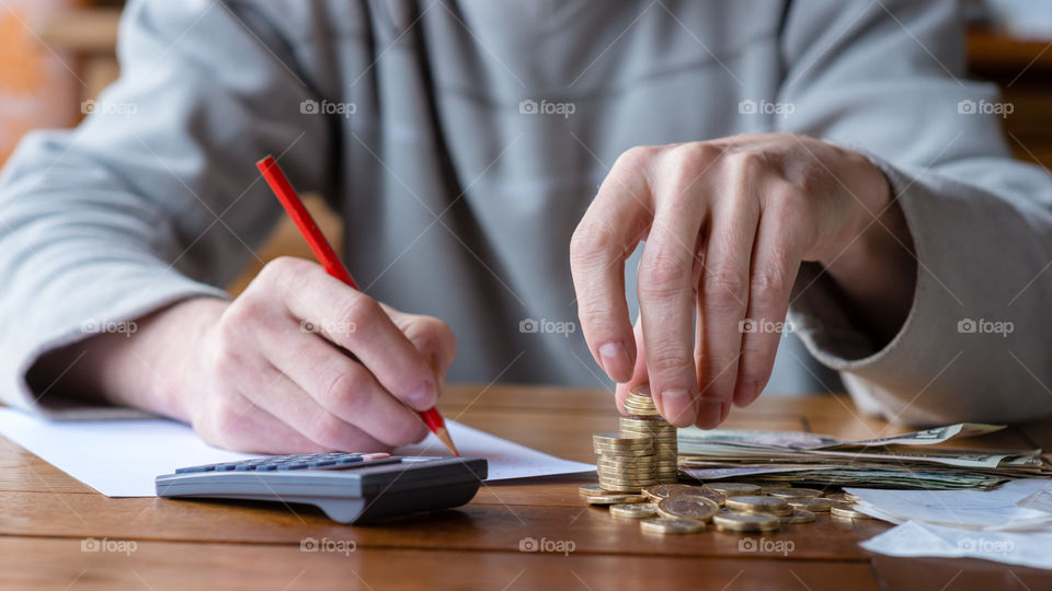 close up man with calculator counting, making notes and writing in notebook. Stacked coins arranged at desk. Savings finance concept.