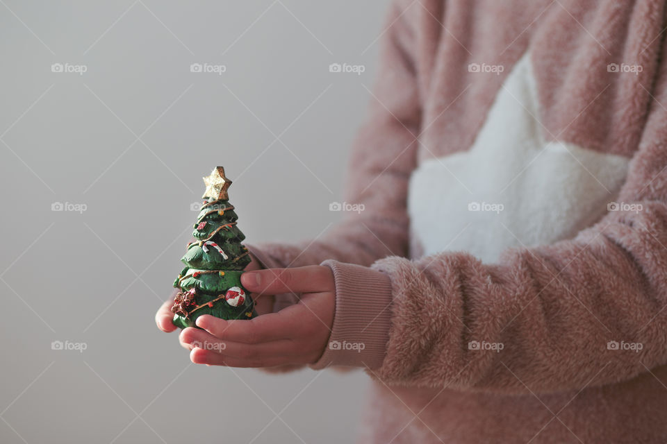 Close shot of young girl wearing warm sweater holding Christmas tree figurine
