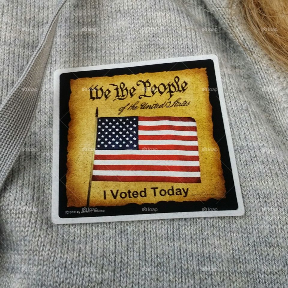A rectangle American flag on a square I voted today sticker on the sweater of a woman closeup