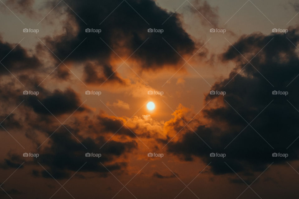 the sun surrounded by dark clouds with a beautiful orange sky before it's time to go down