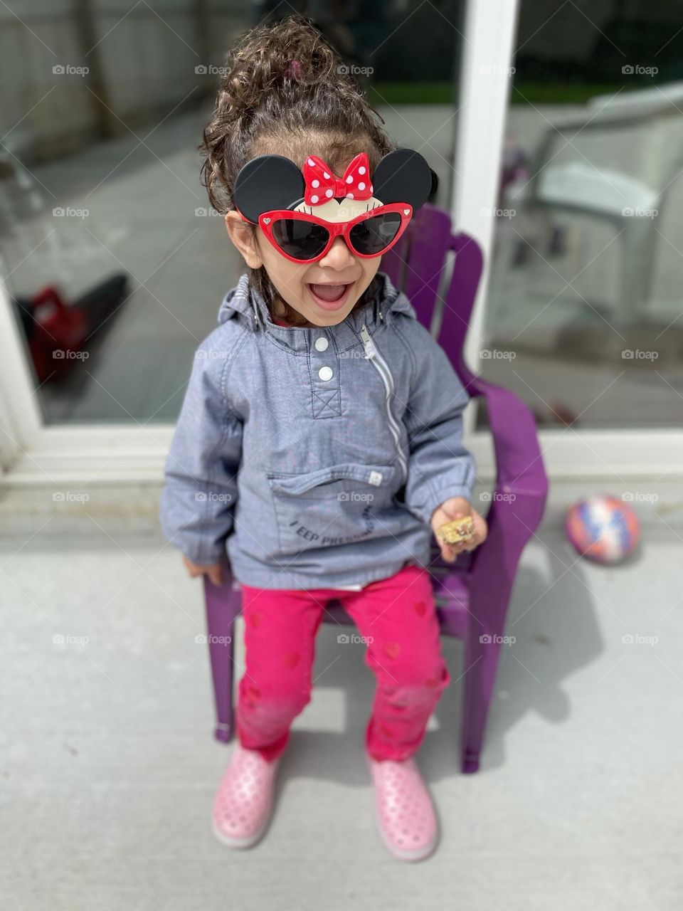 Toddler girl is excited to be wearing Minnie Mouse sunglasses, pure joy of a toddler being outside, enjoying the spring weather with kids, sitting outside with sunglasses on 