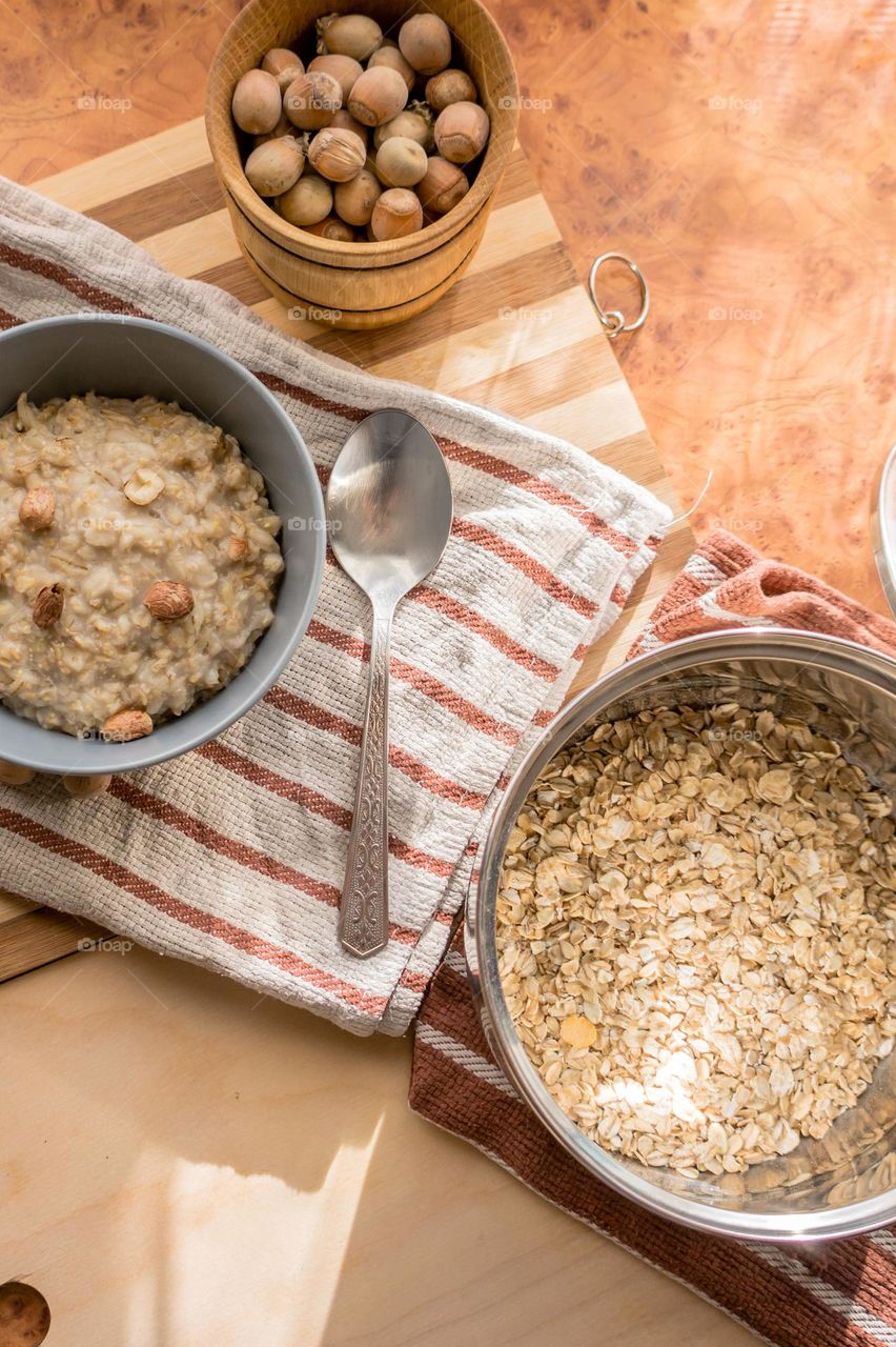 Cooked oatmeal in a deep gray plate with hazelnuts and honey.