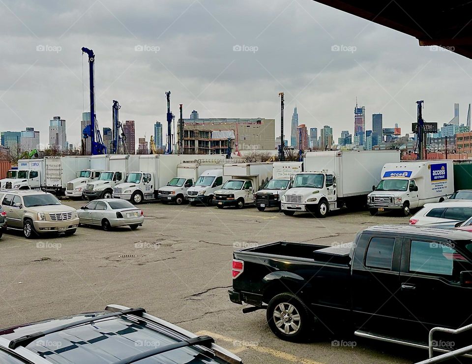 This is the parking lot of „ACCESS Storage“ on „Review Avenue“ near „Borden Avenue“, the BQE and „Dutch Kills“. A fleet of company trucks is parked here ready to go. In the distance we can see the „Manhattan“ skyline. 2023. Hypnotic Productions