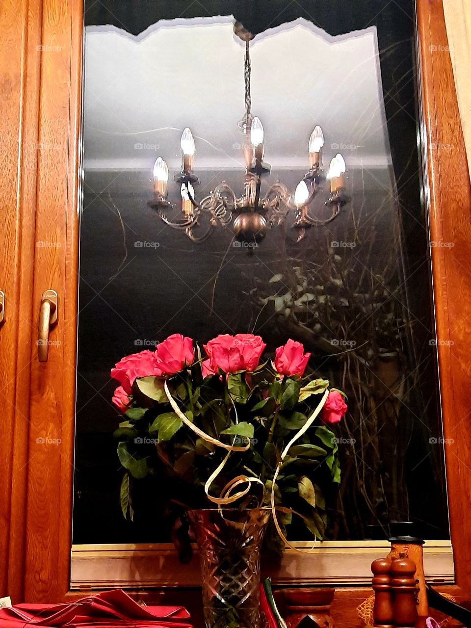 bouquet of red roses  on windowsill with a reflection of chandelier in the glass