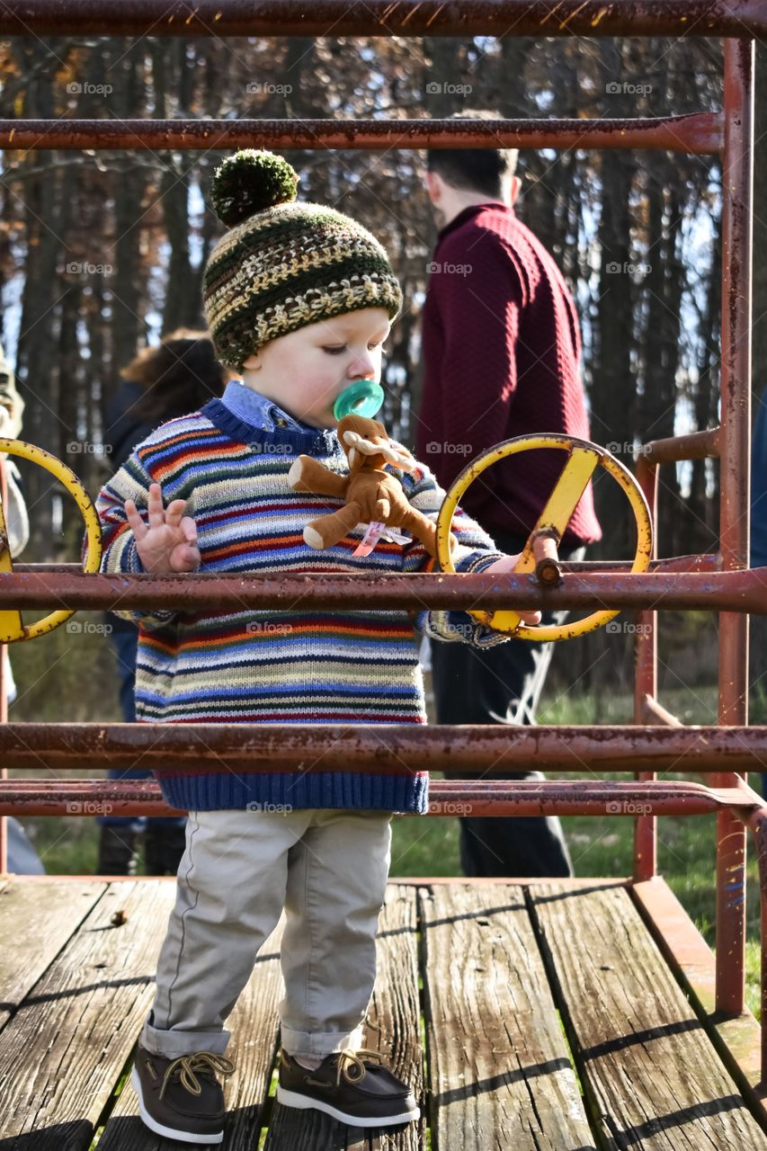 Cute toddler boy in knit sweater and cap playing outdoors 