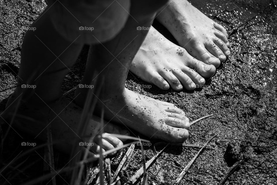 Black and white close up of kids feet playing in the mud alongside the river on a hot summer day 