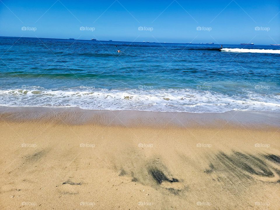 Beach waves crash to shore, sitting in the sand watching surfers out in the distance.