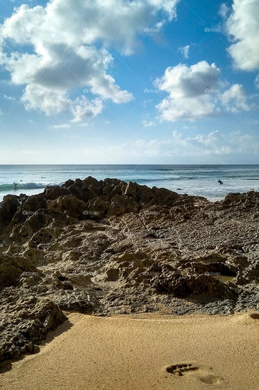 Rocks on the edge of a white sand beach with people's footprints in close-up angle view