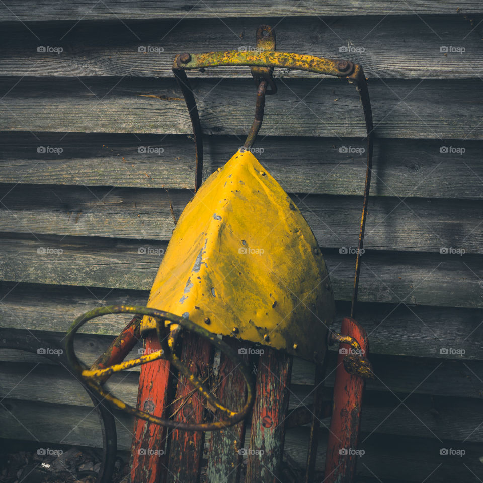 Rusty sled beside wooden wall