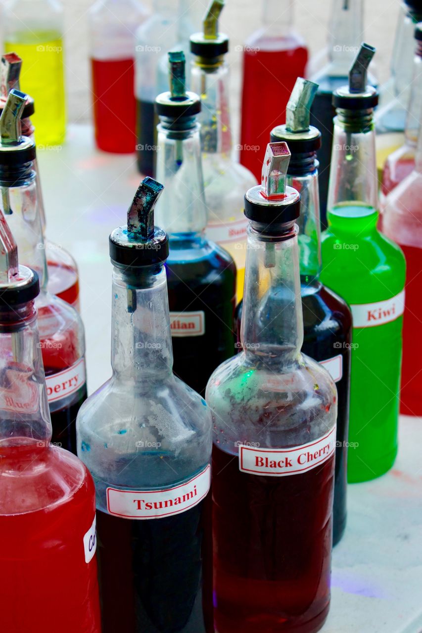 Bottles of assorted, exotic flavorings for sno-cones outdoors on a round white table  