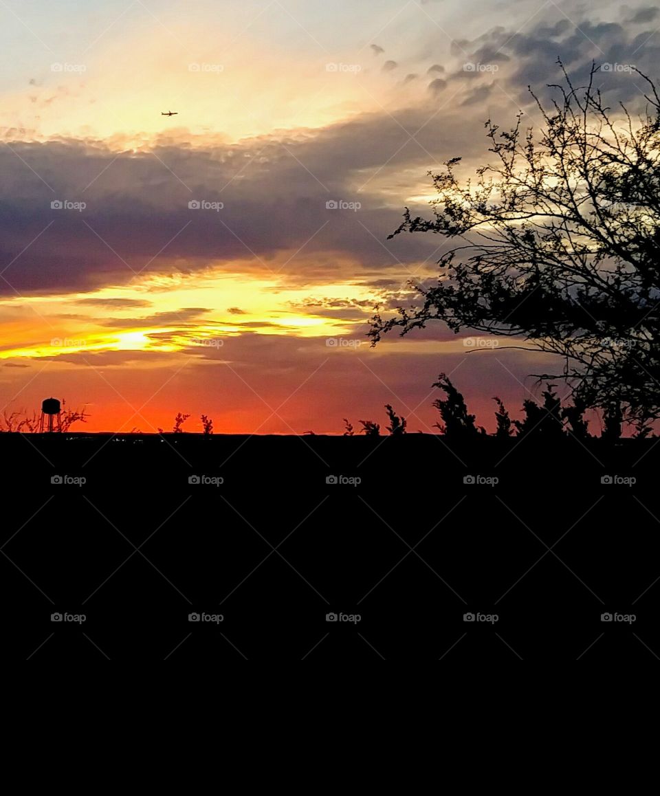 Sunset - water tower in view and at a distance a commercial airliner plane.