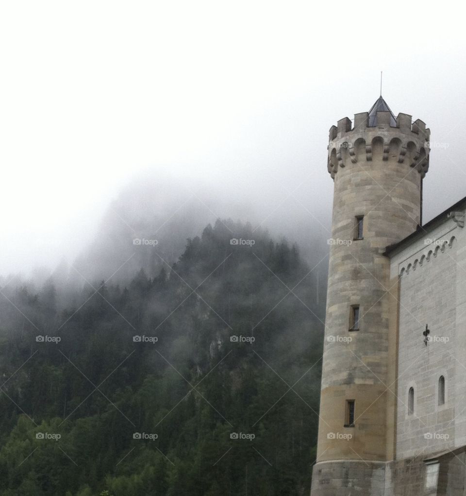 A castle tower looming out of the misty fog, the deep green mountainside in the background
