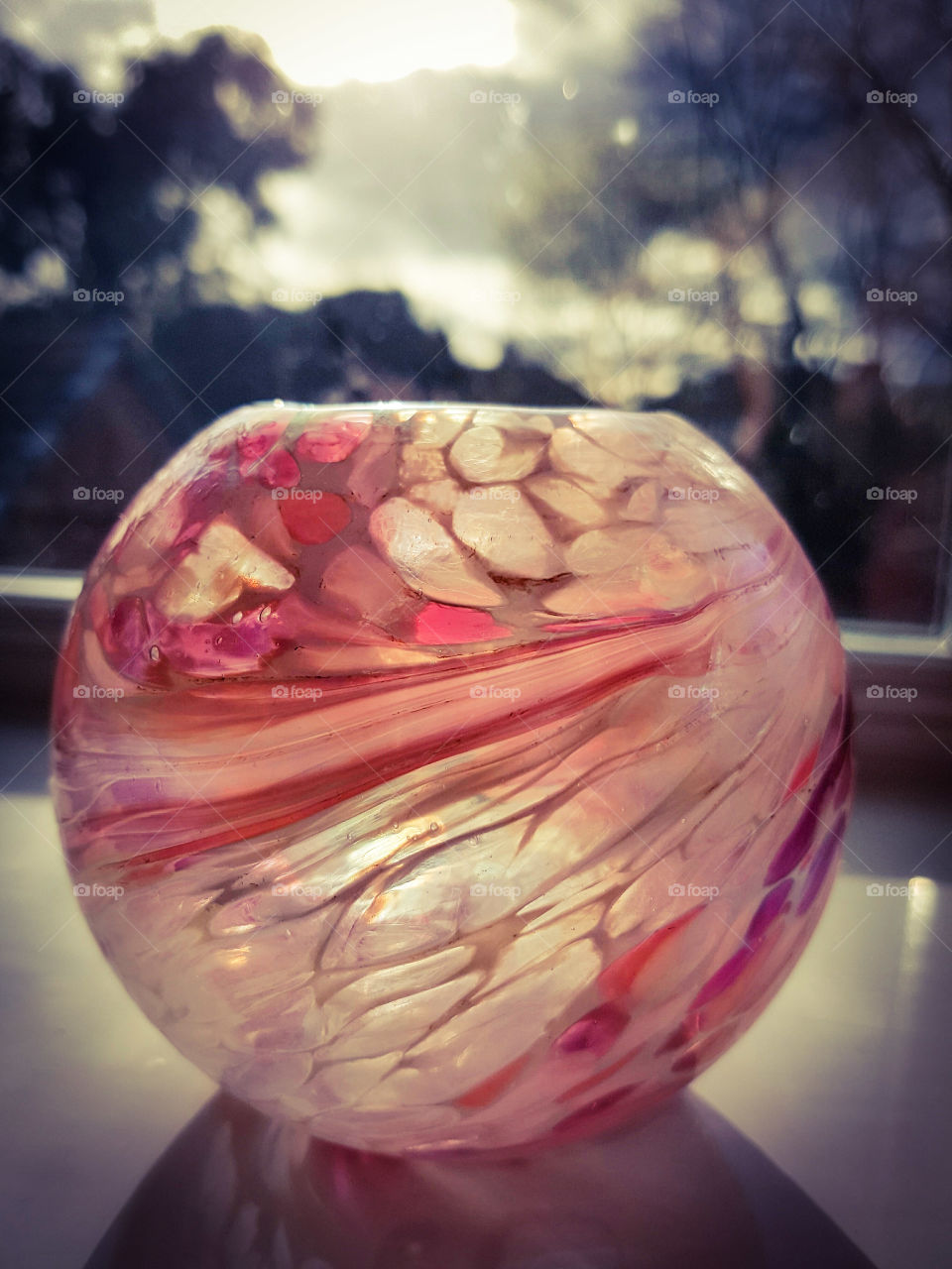 Beautiful pink glass ball. swirls of multiple shades of pink glass with the sun shining through the glass ball on a window ledge.