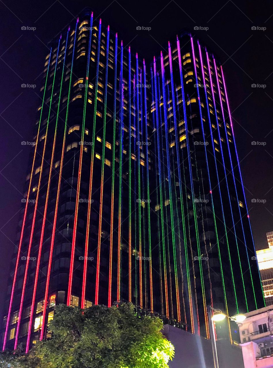 View from below on the tall skyscraper with multicolor neon lamp lights along the building facade 