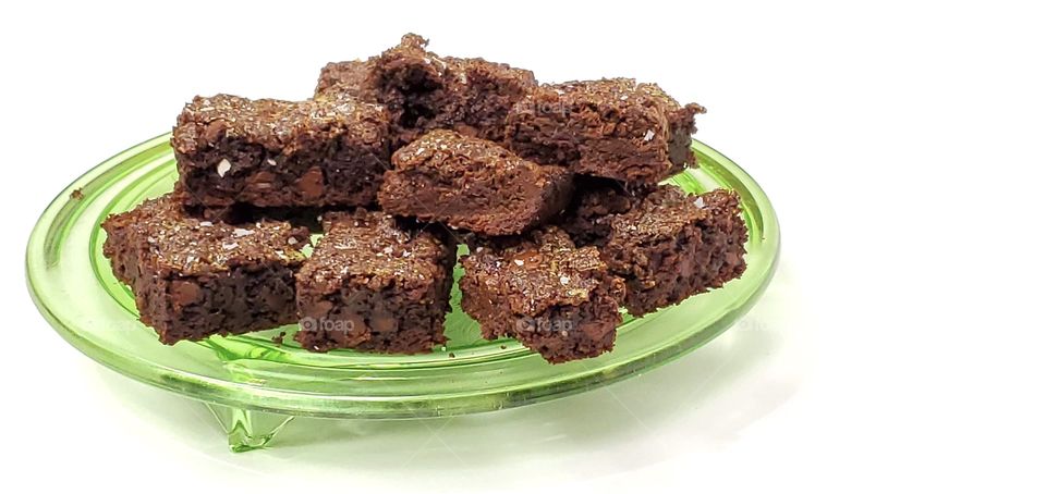 Chocolate brownies on a green glass plate with a white background 