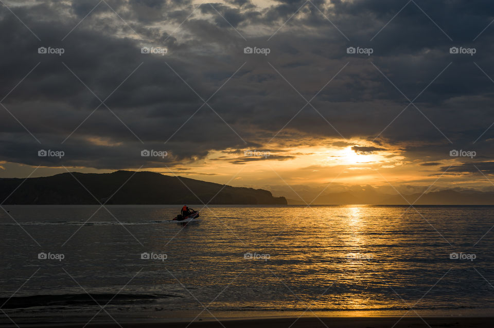 Kamchatka landscape.  A man on a boat with a motor floats on the sea towards sunset