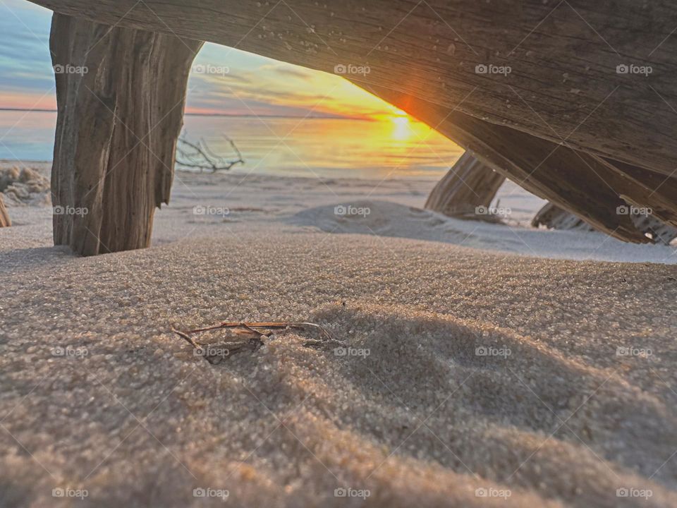 A descending sunset reflection off the waters surface. Taken from underneath a buried log in the sugary white crystal sand